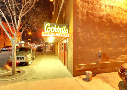 A nighttime street view of Monte Vista Lounge with a glowing "Cocktails" sign and parked cars nearby.