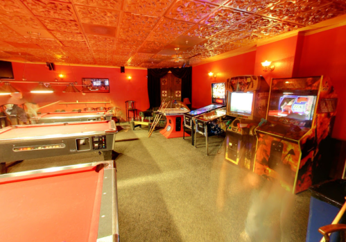 A vibrant game room featuring pool tables, pinball machines, and arcade games against a red wall backdrop.