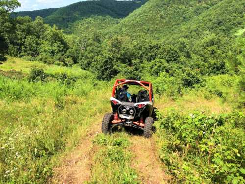 A red off-road vehicle on a grassy trail surrounded by lush green hills and trees.