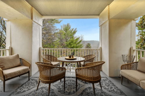 Cozy balcony with wicker chairs, a round table, and scenic views of trees and mountains in the background.