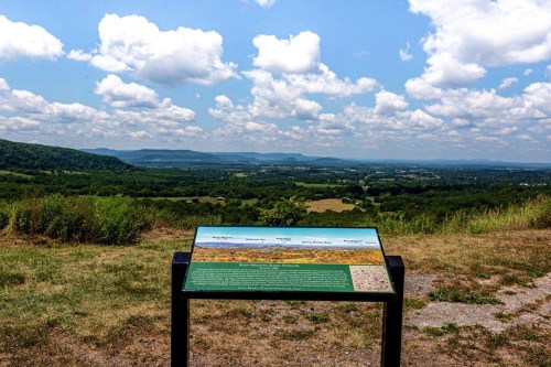 A scenic view of rolling hills and valleys under a partly cloudy sky, with an informational sign in the foreground.
