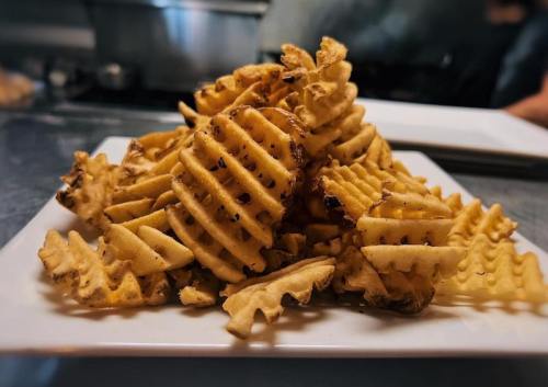 A plate of golden, crispy waffle fries stacked high, served in a restaurant setting.