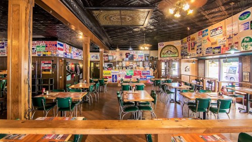 A cozy restaurant interior with wooden tables, green chairs, and vintage signs adorning the walls.