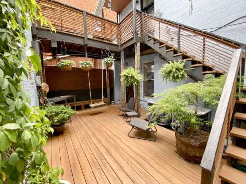 A cozy outdoor patio with wooden decking, hanging plants, a swing, and seating areas surrounded by walls and stairs.