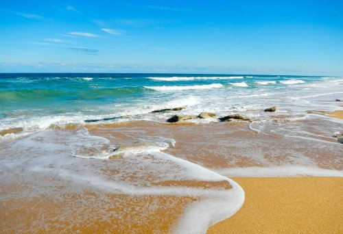 A serene beach scene with gentle waves lapping at the sandy shore under a clear blue sky.