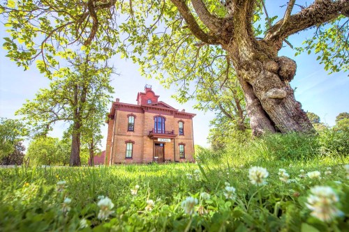 A historic brick building surrounded by lush green grass and trees, with a clear blue sky above.