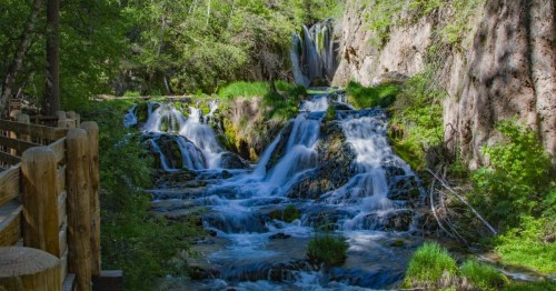 Views of a serene waterfall in SD, cascading over limestone rocks inside a dense forest.