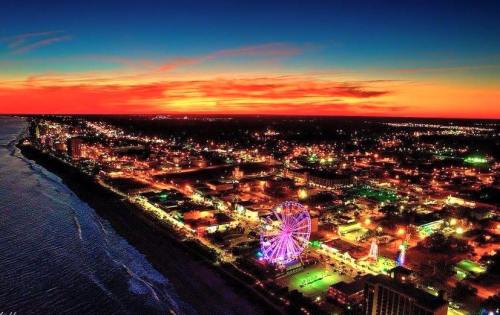 A vibrant sunset over a coastal city, featuring colorful lights and a ferris wheel along the shoreline.