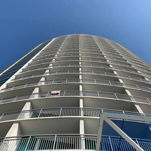 A tall, modern building with multiple balconies against a clear blue sky.