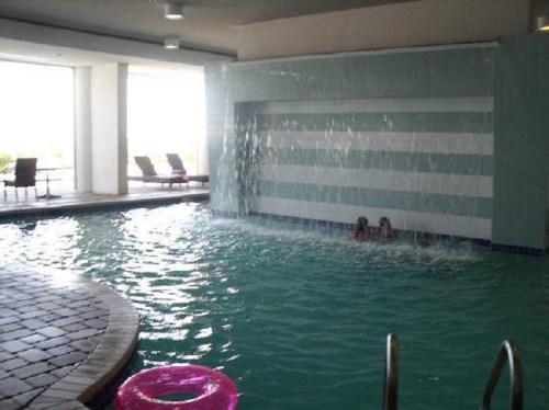 Indoor pool with a waterfall feature, lounge chairs in the background, and two people swimming.