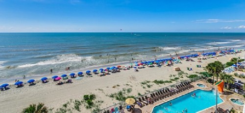 A sunny beach scene with colorful umbrellas, people enjoying the water, and a pool area in the foreground.