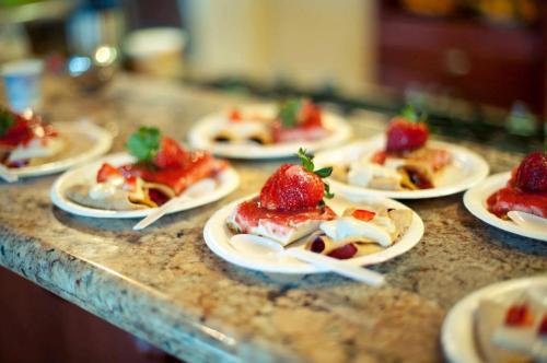 Plates of dessert topped with strawberries and sauce, arranged on a countertop.