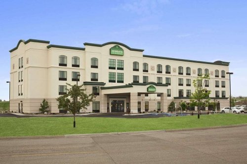 A modern, four-story hotel with a green and white facade, surrounded by grass and a clear blue sky.