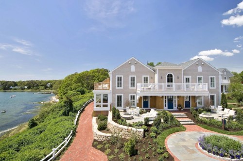 A beautiful waterfront home with a landscaped yard, patio, and scenic views of the water and greenery.