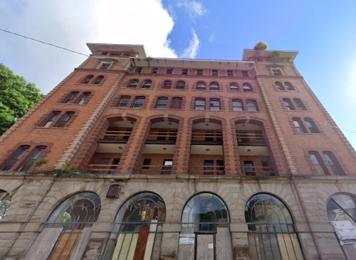 Historic brick building with arched windows and a blue sky in the background, showing signs of wear and neglect.