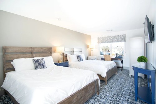 Bright hotel room featuring two beds, a desk, and a window with patterned curtains. Modern decor and cozy atmosphere.