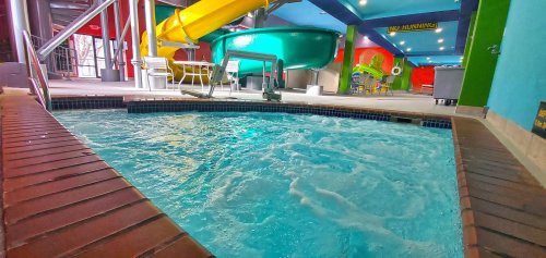 Indoor water park featuring a pool with a water slide and colorful walls. Bubbles and splashes are visible in the water.