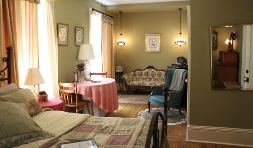 Cozy room featuring a bed, vintage furniture, a table with a pink tablecloth, and warm lighting.