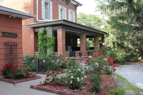 A charming brick house with a porch, surrounded by a colorful rose garden and lush greenery.