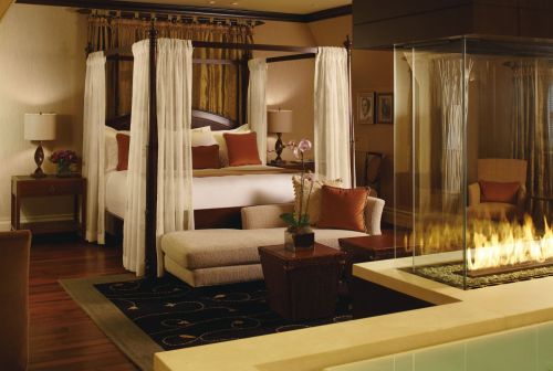 Luxurious hotel room featuring a four-poster bed, cozy seating area, and a modern fireplace. Elegant decor throughout.