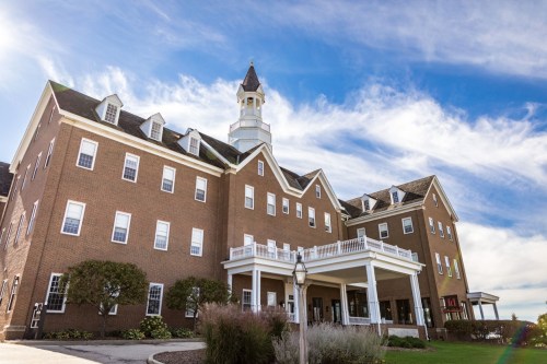 Historic brick building with a tower, surrounded by greenery and under a blue sky with clouds.