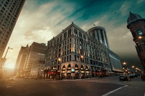 A city street scene featuring historic buildings under a dramatic sky at dusk.