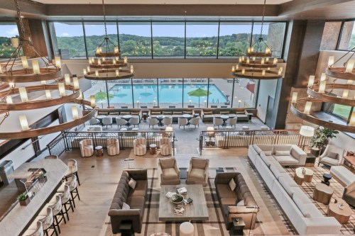 A spacious, modern lobby with large windows overlooking a pool and outdoor seating, featuring stylish furniture and lighting.
