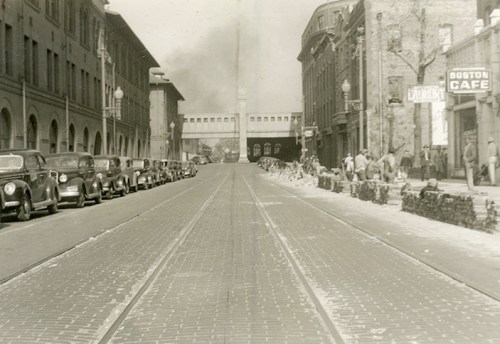 A historic street scene with vintage cars, buildings, and a clock tower in the background, evoking a bygone era.