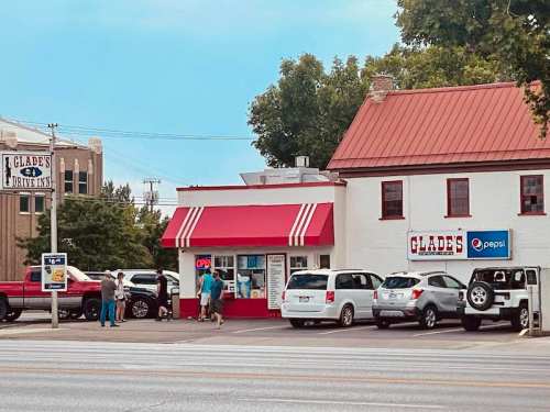 A small drive-in restaurant with a red awning, cars parked outside, and people entering the establishment.