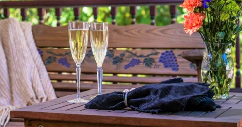 Two champagne flutes on a wooden table, accompanied by a black napkin and a vase of colorful flowers.