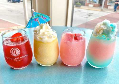 Four colorful drinks in glasses, featuring a red, yellow, pink, and blue beverage, each with garnishes and decorations.