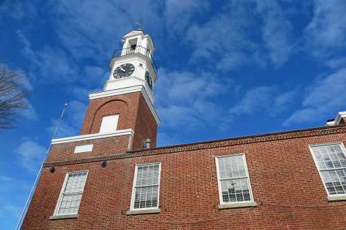 A brick building with a clock tower against a blue sky with scattered clouds.