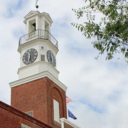 A clock tower with a white facade, featuring a large clock and an American flag, against a cloudy sky.