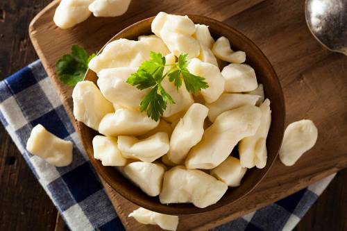 A wooden bowl filled with fresh cheese curds, garnished with a sprig of parsley, on a checkered cloth.