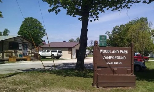 Sign for Woodland Park Campground in Grand Marais, with buildings and trees in the background on a sunny day.