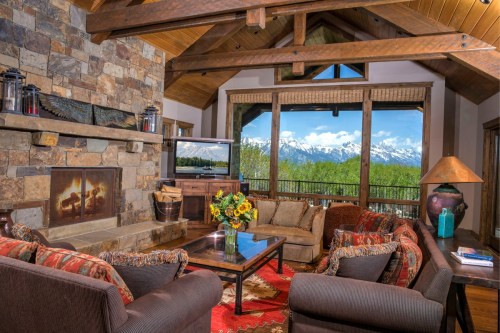 Cozy mountain lodge interior with stone fireplace, comfortable seating, and large windows showcasing snowy peaks.