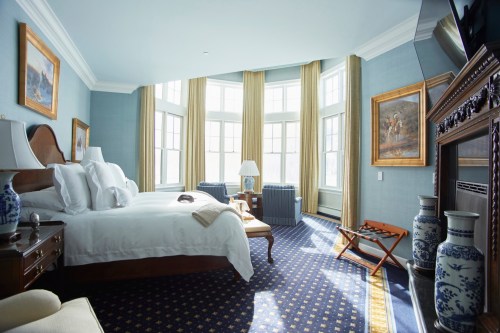 Bright, elegant hotel room with a king bed, large windows, blue decor, and classic furnishings.