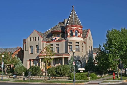 Victorian-style house with a turret, decorative trim, and lush greenery, set against a clear blue sky.