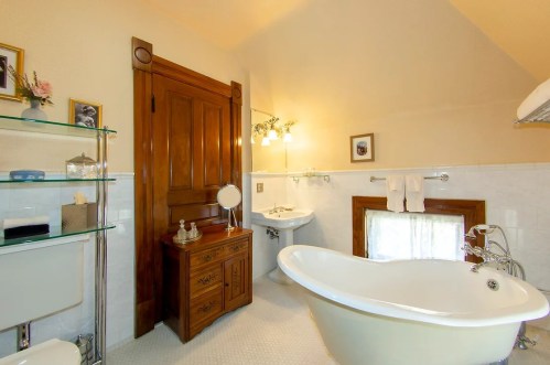 A cozy bathroom featuring a freestanding tub, vintage decor, and a wooden door, with soft lighting and elegant fixtures.