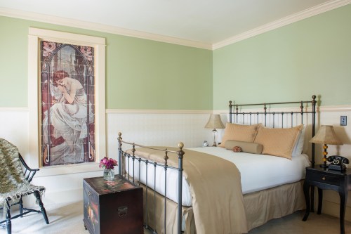 Cozy bedroom with a green wall, vintage bed, decorative window, and a small table with flowers and a classic phone.