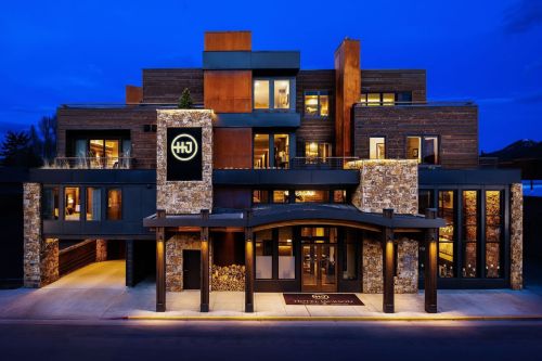Modern hotel exterior at dusk, featuring stone and wood elements, with a welcoming entrance and illuminated signage.