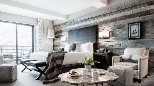 A modern hotel room featuring a king bed, wooden accent wall, seating area, and a coffee table with snacks.