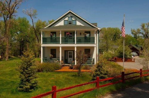 A two-story house with a porch, surrounded by greenery and a red fence, featuring an American flag in the front yard.
