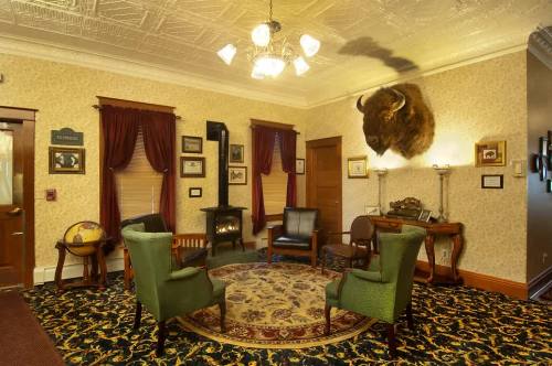 A cozy room with green chairs, a patterned rug, and a bison head mounted on the wall, featuring vintage decor.