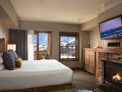 Cozy hotel room with a king bed, fireplace, TV, and mountain views through large windows.