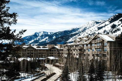 A scenic view of a mountain resort surrounded by snow-covered peaks and trees under a clear blue sky.