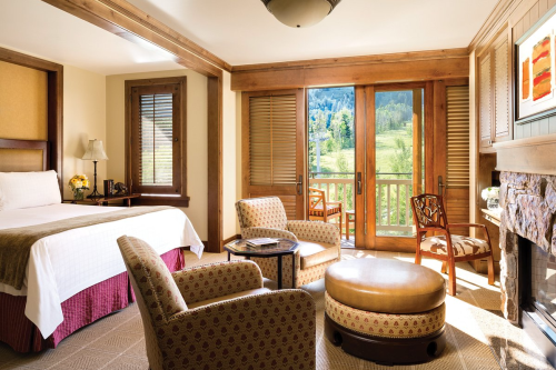 Cozy hotel room with a bed, seating area, and balcony overlooking a scenic view of mountains and greenery.