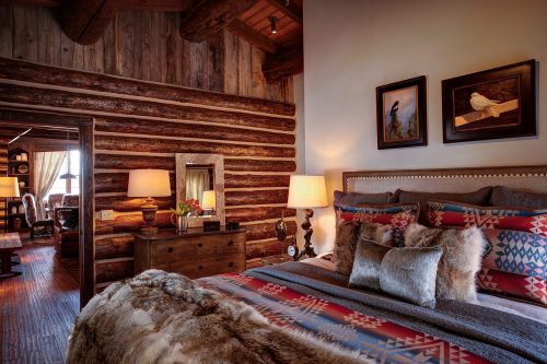 Cozy rustic bedroom with log walls, a patterned bedspread, and warm lighting from bedside lamps.