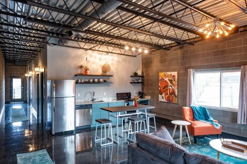 Modern industrial kitchen and living area with stainless steel appliances, a dining table, and colorful decor.