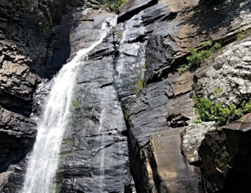 A tall waterfall cascading down rugged, rocky cliffs surrounded by greenery.